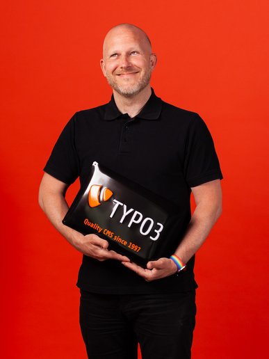 Andreas Beutel hält ein TYPO3 Schild selig lächelnd in seiner Hand