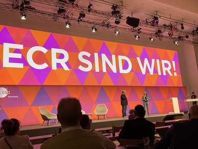Bühne mit zwei Rednern auf dem ECR Tag 2023. Im Hintergrund ist der Schriftzug „ECR sind wir“ zu lesen.