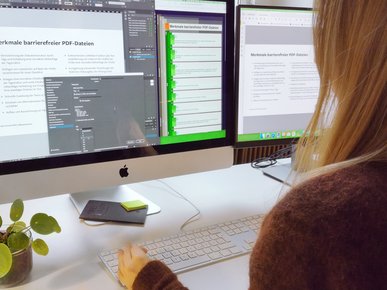 Blick über die Schulter von Kathrin Scholz, die am Monitor barrierefreien InDesign-Dateien anlegt