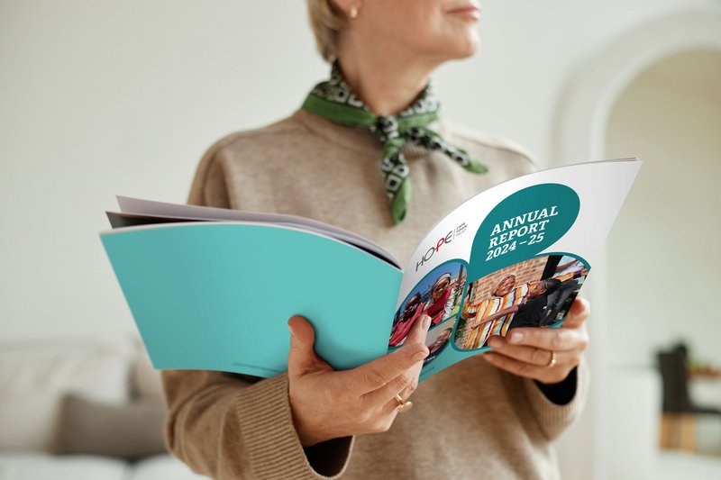 Frontalansicht einer Frau, die den aufgeschlagenen Jahresbericht von HOPE Cape Town in den Händen hält