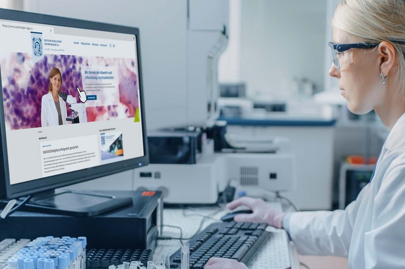 Eine Frau in einem Laborkittel sitzt vor einem Rechner und sieht sich die Website der DGP an