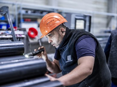 Fachkraft kontrolliert mit einer Taschenlampe ein Zylinderrohr an einer Schäl- und Rollieranlage.