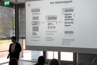 Ausschnitt eines Workshoptags an der Technischen Universität Dortmund, Publikum sitzt vor weißer Leinwand auf der Seitentypen einer Webseite dargestellt werden  